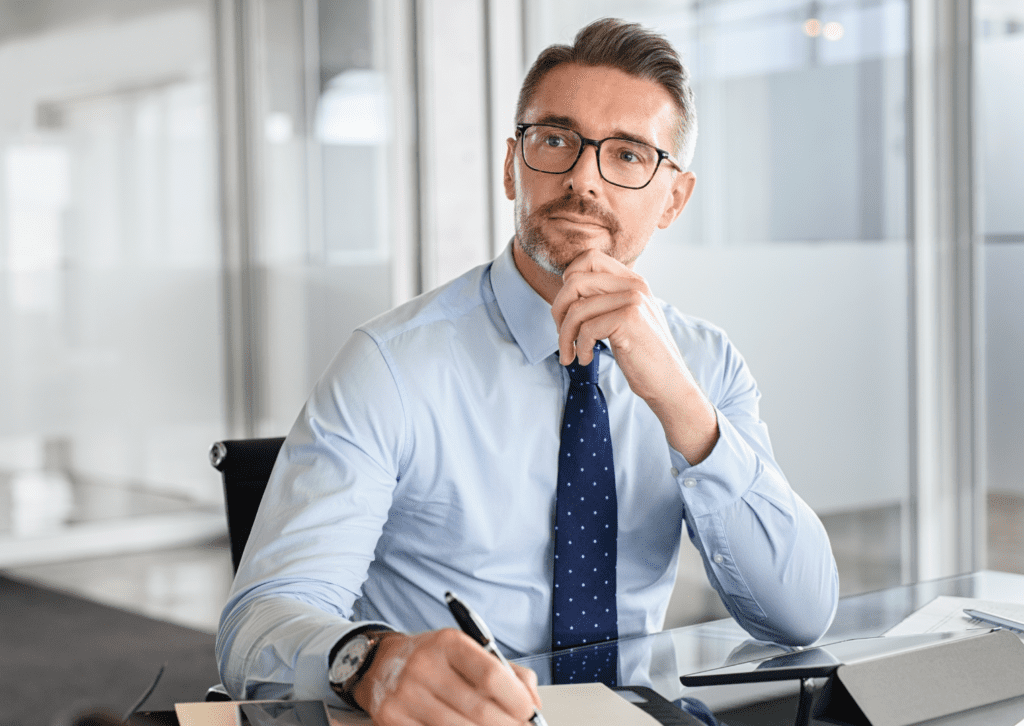 Businessman of a small business inside his office thinking with his hand on his chin thinking about digital marketing strategies