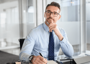 Businessman of a small business inside his office thinking with his hand on his chin thinking about digital marketing strategies